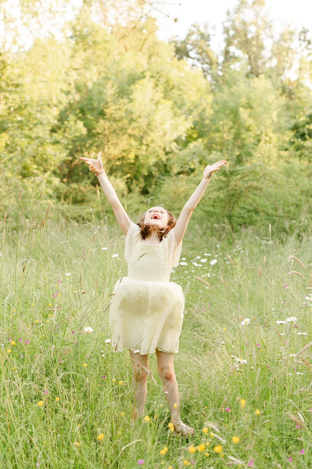 A happy toddler girl in a yellow dress dances and plays in some wildflowers after meeting with NorthWest Nannies