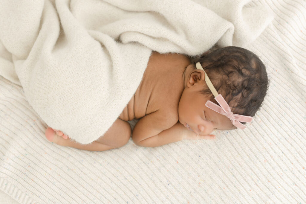 Top view of a newborn baby sleeping peacefully on belly with some cream blankets draping gently across her lower body.