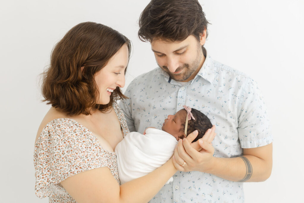 Mom and Dad holding newborn baby between them at studio newborn session.