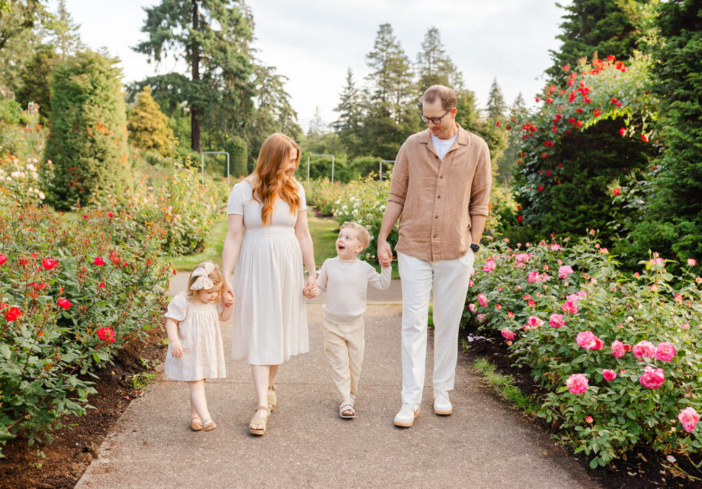 Rose garden family photos in Portland, Oregon. Family of four - mom, dad, brother and sister hold hands while walking together through the International Rose Test Gardens.